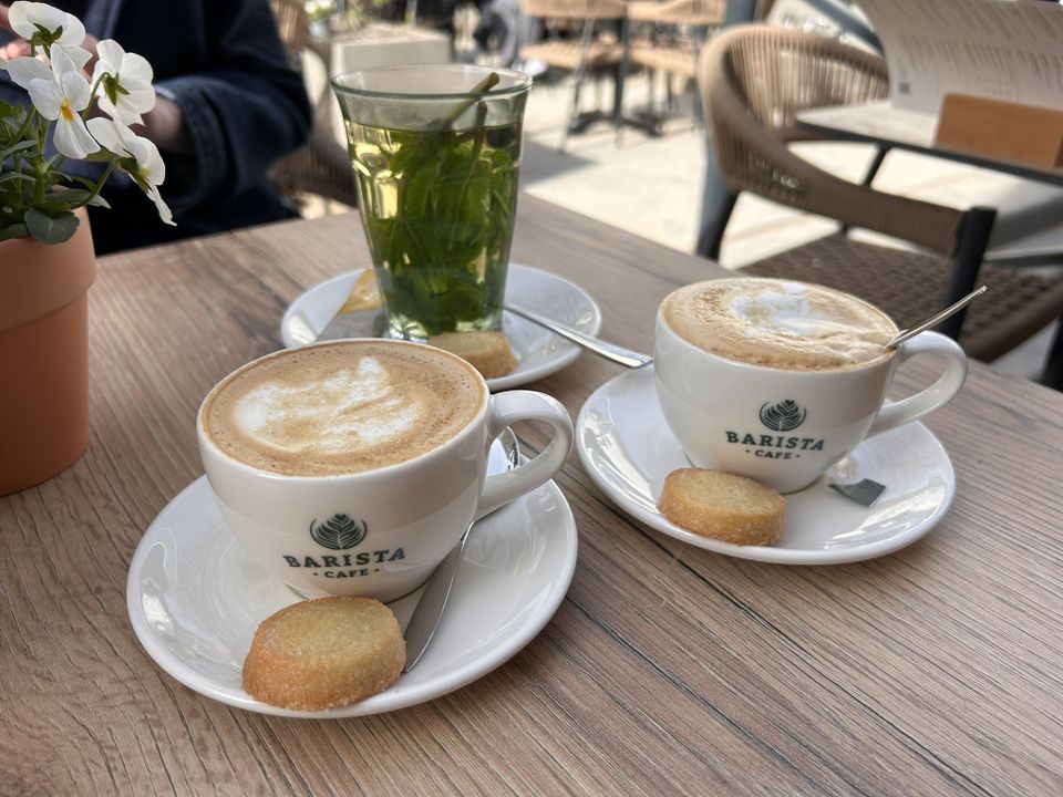 Horecaterras Barista Café Woerden in Woerden, Groene Hart, met cappuccino’s en verse muntthee op houten tafel, koekje op schotel en zonnige setting voor een koffie moment in de binnenstad.