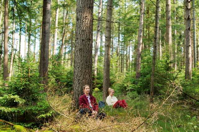 2 mediterende vrouwen leunend tegen de stam van een boom in de Drentse natuur.