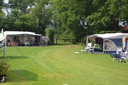 Groot groen grasveld met aan de zijkanten 2 caravans met voortenten en zitjes.