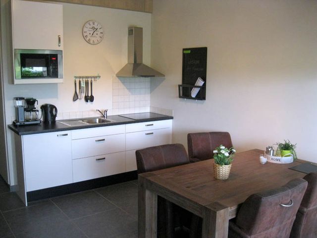 Vakantiehuisje met een wit keukenblok en een eettafel met vier stoelen.