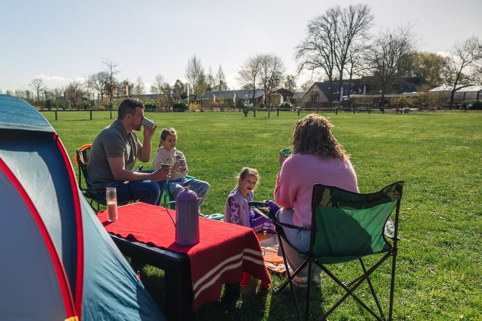 Een gezin zit voor een blauw, rode tent in een grasveld.