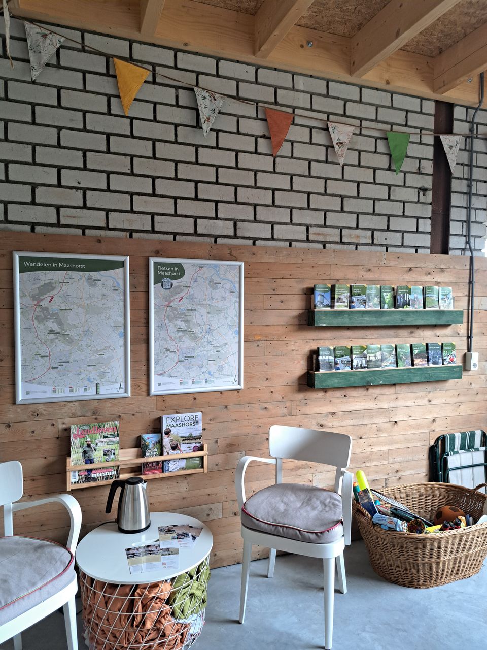 Informatiehoek met stoelen en tafel, wandkaarten ‘Wandelen in Maashorst’ en ‘Fietsen in Maashorst’, en planken met folders en brochures.
