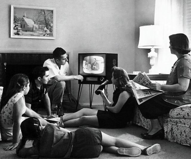 Zwart wit foto waarop een gezin samen naar een televisie uitzending kijkt