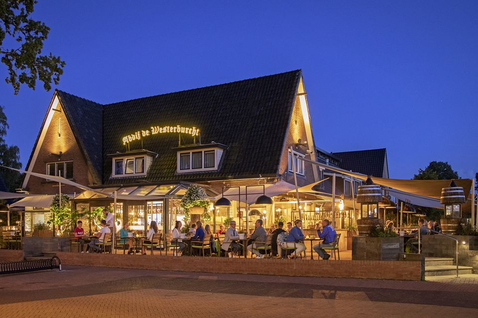 Mensen genieten in de avonduren van een hapje en een drankje op het verlichte buitenterras van hotel restaurant.