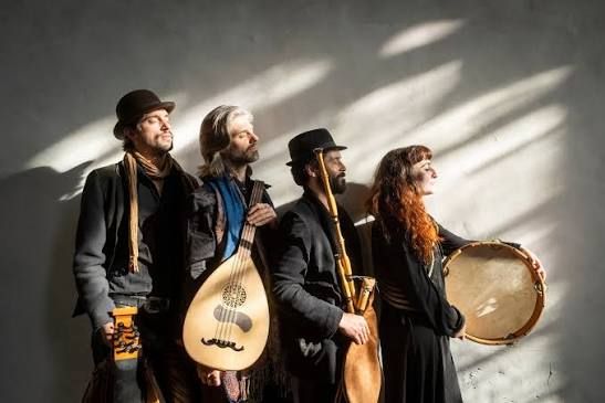 Foto van vier artiesten, staande met hun instrumenten in folk-kleding en met hun ogen dicht.