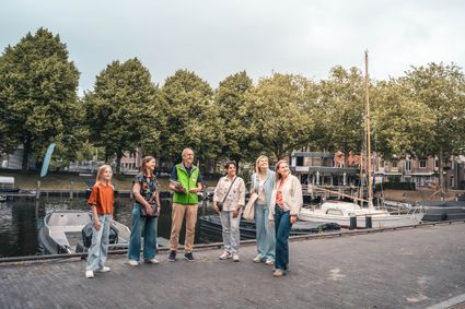 Historische stadswandeling met een Gildegids langs de haven in Woerden, Groene Hart. Groep bezoekers ontdekt de monumentale binnenstad en haven tijdens een begeleide rondleiding met historische schepen en bomen langs het water.