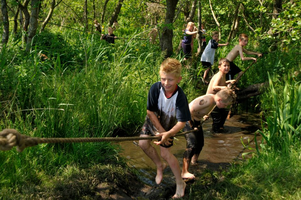 Kinderen die aan een touw hangen in het water in het kameleondorp Teherne