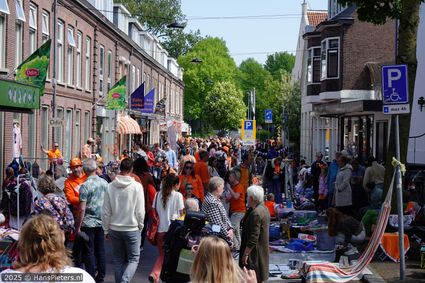 Straatevenement Koningsdag in Woerden, Groene Hart, drukbezochte vrijmarkt met kraampjes, kleedjes en verkopers in oranje kleding in een winkelstraat in de historische binnenstad.
