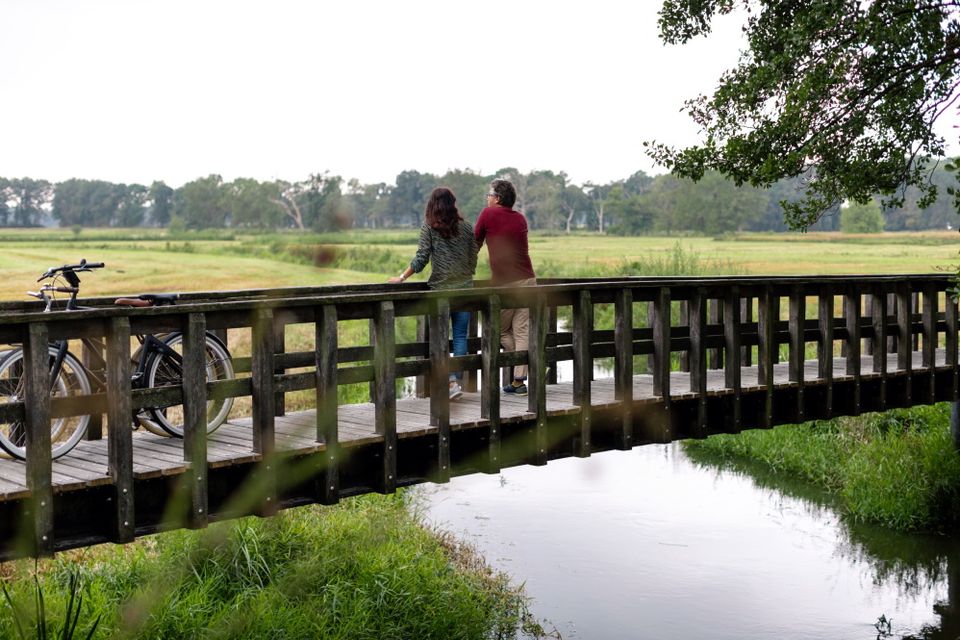 Ein Mann und eine Frau haben ihre Radtour pausiert und genießen von einer Brücke aus den Blick auf die Natur.