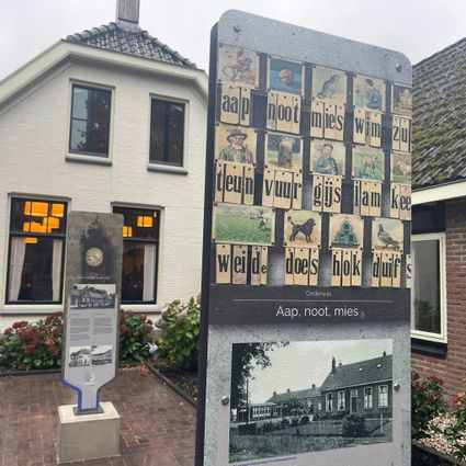 Aap noot mies afbeelding. Onderdeel van de expositie Het Verhaal van Kolonie Wilhelminaoord. Op de achtergrond Ons Dorpshuis in Wilhelminaoord.