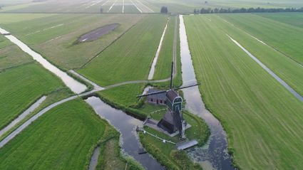 Luchtfoto van de Cabauwse Molen in Lopik: historische poldermolen tussen uitgestrekte groene weilanden en sloten, omgeven door waterlopen en kleine bruggetjes.