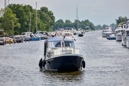 Er vaart een jacht in de vaart van Delfstrahuizen. Op de achtergrond is de vaart te zien en aan beide zijkanten meerdere vastliggende boten.