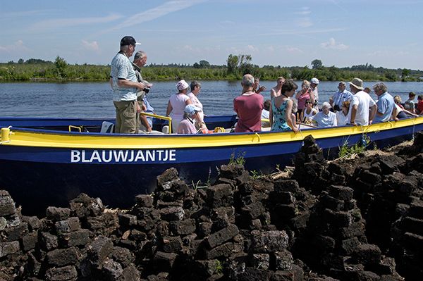 boot 'Blauwjantje' met mensen en ligt nog aan de oever. Mensen gaan een vaartocht Turf en smederijmuseum doen