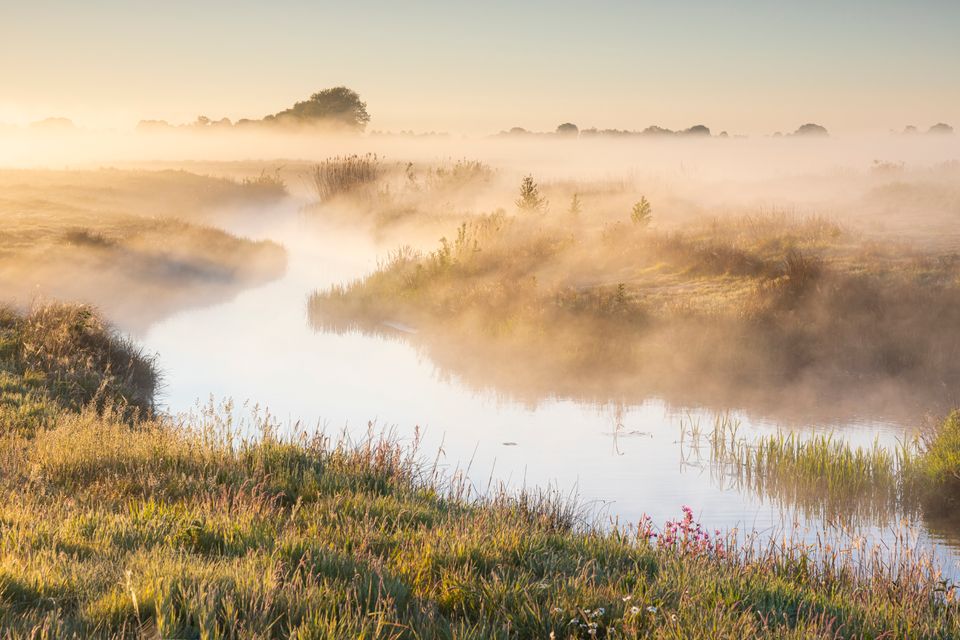 Een slingerend beekje met dauw die langzaam van het omliggende land verdwijnt.