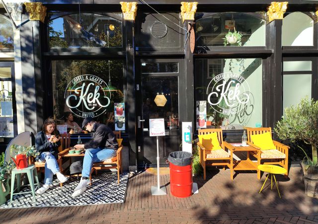 Man en vrouw die koffie drinken op de buitenzitplaatsen van KEK in Delft Centrum