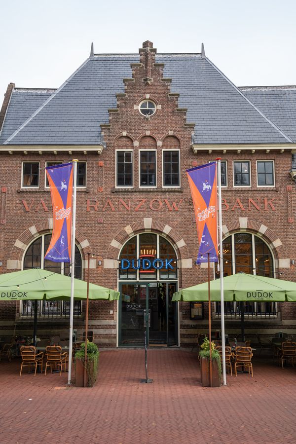 De imposante bakstenen gevel van Dudok Arnhem met een sfeervol terras voor gasten om te genieten. -