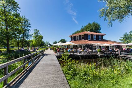 Restaurant Buitenplaats Kameryck in Kamerik, Groene Hart, met zonnig terras vol gasten aan het water, houten brug en groen landschap rondom.