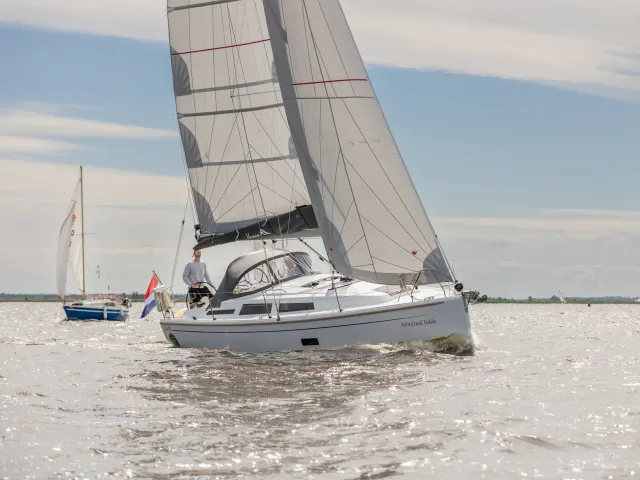 Een kajuitzeilboot zeilt op het water met twee personen aan boord en op de achtergrond nog een zeilboot.