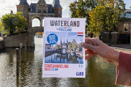 iemand houd boekje met stadswandeling sneek van waterland van friesland vast 
met waterpoort op de achtergrond