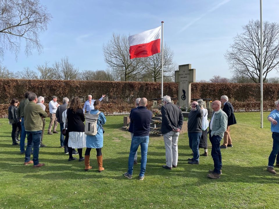 Groep mensen staat in cirkel rondom een oorlogsmonument ter ere van Poolse soldaten uit de Tweede Wereldoorlog. Poolse vlag wappert.