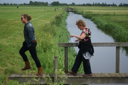 Wandelroute, Boerenlandroute – Balkengatroute, Zoeterwoude, Groene Hart, twee wandelaars die een houten overstap over een sloot passeren in het open polderlandschap met graslanden en watergangen langs de route.