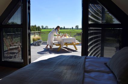 Uitzicht vanuit de slaapkamer van B&B Bedje in de Polder in Montfoort, met openslaande deuren naar een terras waar een ontbijt wordt klaargezet, uitkijkend over de groene weilanden van het Groene Hart.