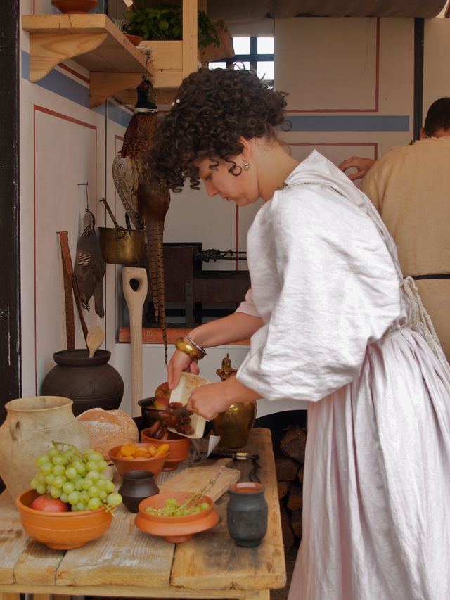 Een vrouw in een witte togajurk bereidt het eten in roodbakken aardewerk.