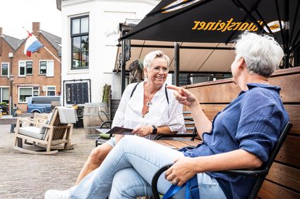 Accommodatie Torentje aan de IJssel in Montfoort, Groene Hart, buitenzitje aan de kade met twee bezoekers in gesprek onder parasol, historisch straatbeeld aan de Hollandse IJssel.