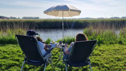 Twee mensen op campingstoeltjes aan het water van de achterkant gefotografeerd op Camping De Finne in Reahûs.