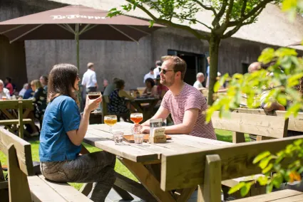 Twee mensen genieten in het zonnetje aan een picknicktafel op het terras van Abdij Koningshoeven in Berkel Enschot