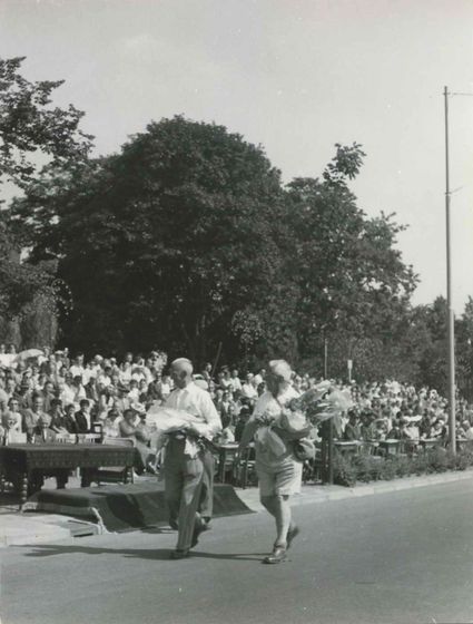 Op de vierde dag van de 40e Vierdaagse passeren twee burgerdeelnemers het erepodium aan de St. Annastraat. Uiterst links (achter de tafel) Ir. C. Staf en marsleider J.N. Breunese.