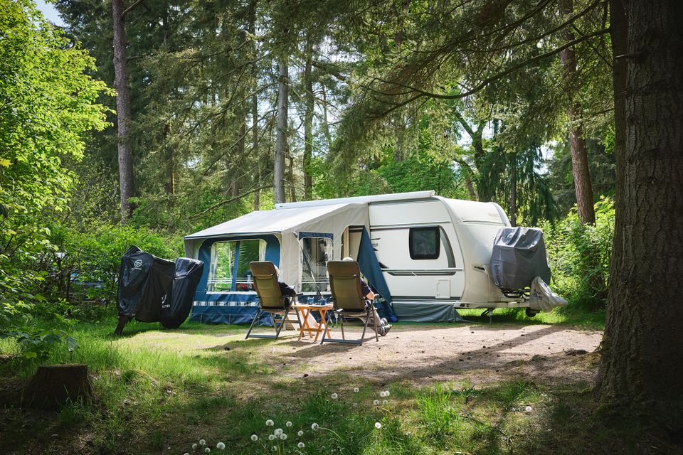 Een caravan met twee mensen op campingstoeltjes bij Camping De Waps in Oudemirdum.