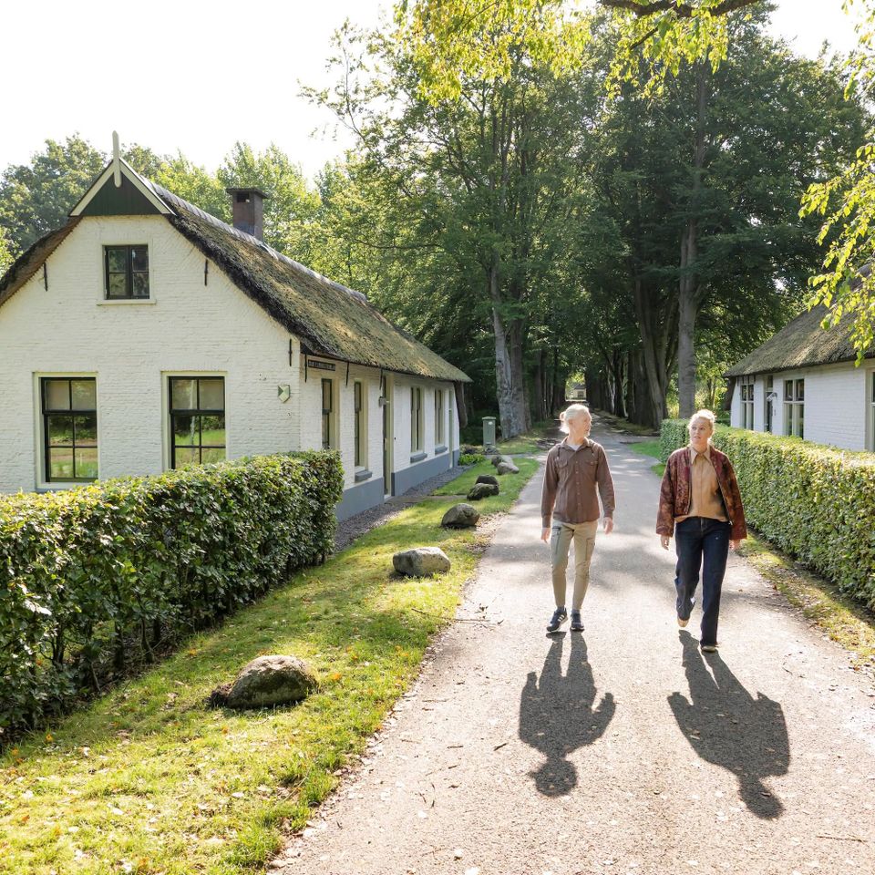 Man en vrouw wandelen op het voetpad tussen de ambtenarenhuisjes in Frederiksoord
