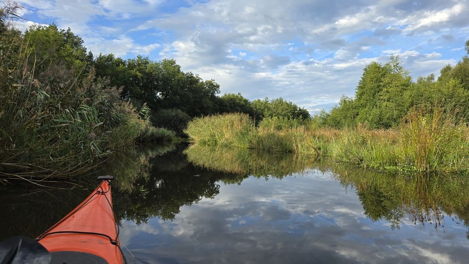 Uitzicht vanuit een kajak op een bocht in de Ruiten Aa, met groene oevers en weerspiegeling in het water. Eigen routebeeld uit september 2026.