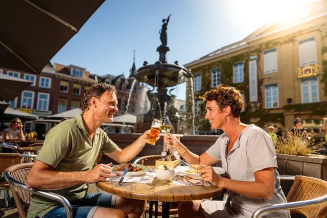 Stel proost op een zonovergoten terras bij de fontein op de Markt in Gorinchem, met op de achtergrond het Gorcums Museum en historische panden.