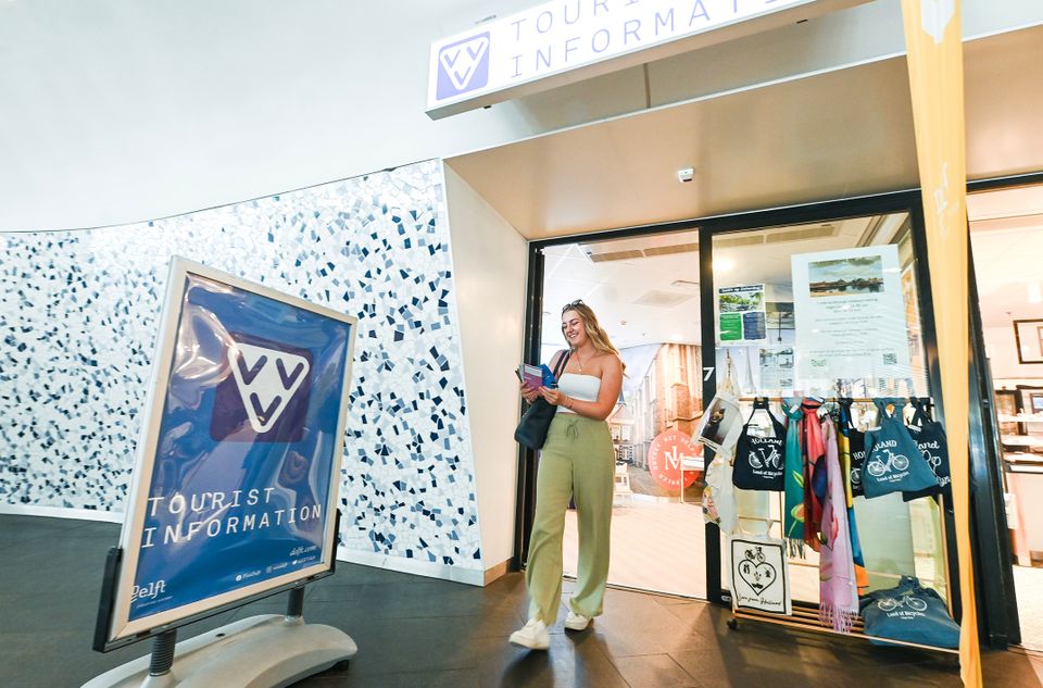 Jongedame loopt uit het VVV Delft met folders in haar hand in de zomer