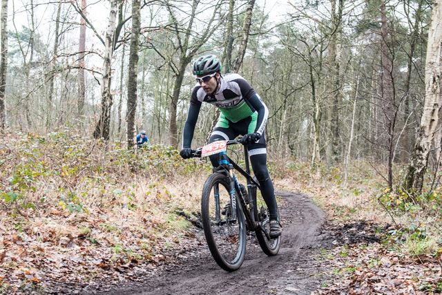 Mountainbiker rijdt over een smal en modderig bospad op de Utrechtse Heuvelrug. De foto laat sportief mountainbiken en actieve natuurbeleving in het bos zien.