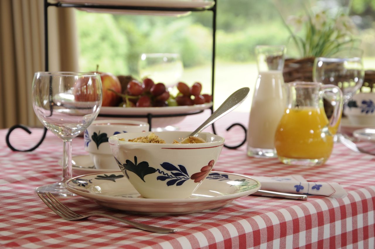 Tafel gedekt met Brabants bont tafelkleed en servies, met een fruitschaal en karaf met jus d'orange en melk.