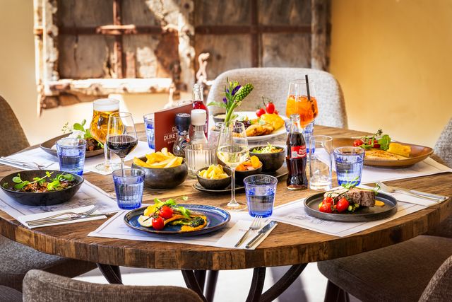 Gedekte ronde tafel in Bistro en Bar De Dijketelg in Oudewater met diverse kleurrijke gerechten, drankjes en glazen, sfeervol verlicht in een warme, landelijke setting.
