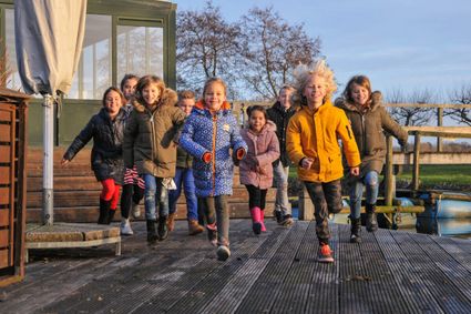 Recreatieboerderij De Boerinn in Kamerik, Groene Hart, met een groep kinderen die buiten over een houten vlonder rent langs het water en polderlandschap.