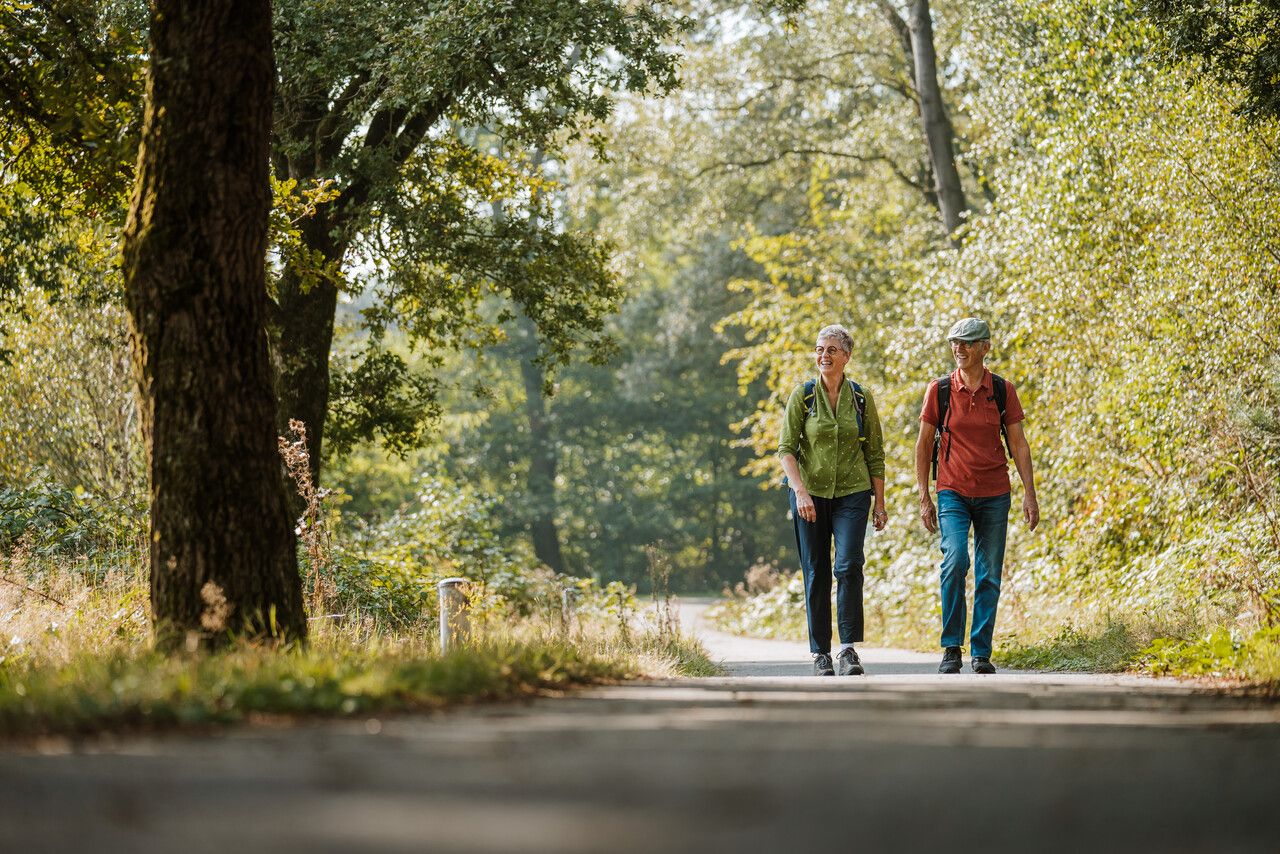 Twee wandelaars, man en vrouw, wandelend door het groen over verhard pad.