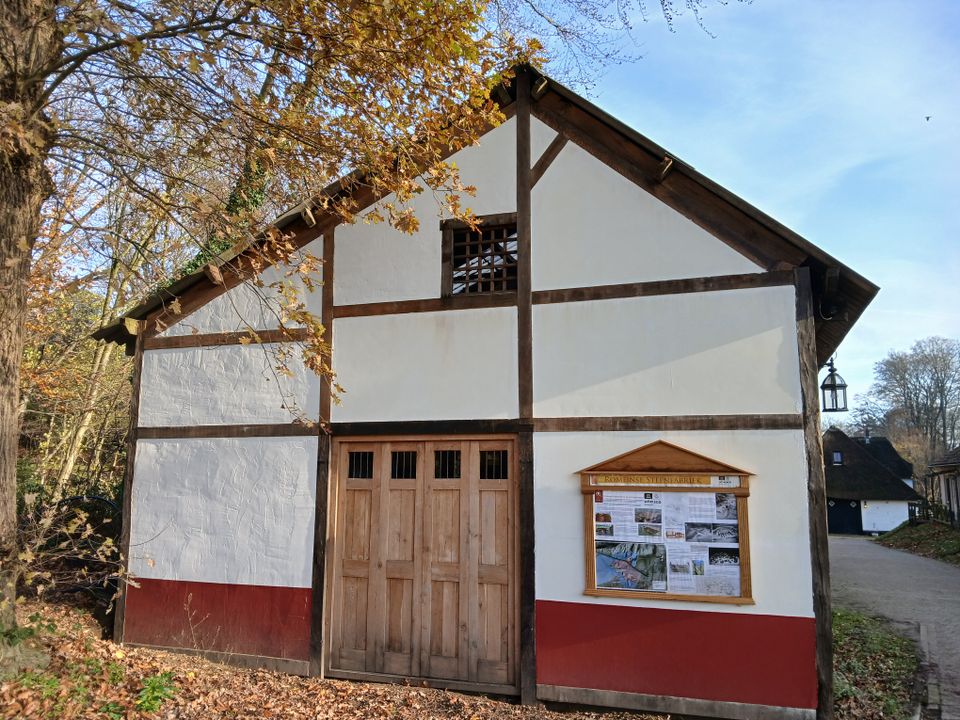 Een vakwerkgevel met rode onderkant, dichte deuren en een informatiebord