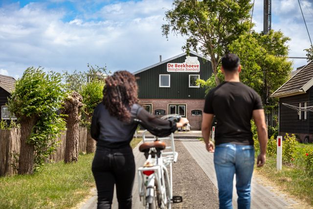 Twee bezoekers wandelen met een fiets richting De Beekhoeve, een biologische boerderij in Kamerik, Utrecht Region