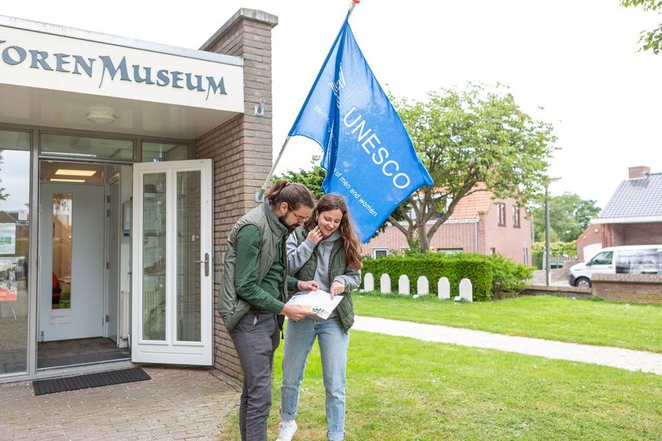 Twee bezoekers voor de ingang van het Torenmuseum aan de Limes. Aan de gevel wappert een Unesco vlag.