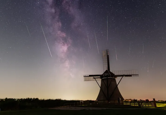 Vallende sterren in de lucht met een molen aan de horizon.