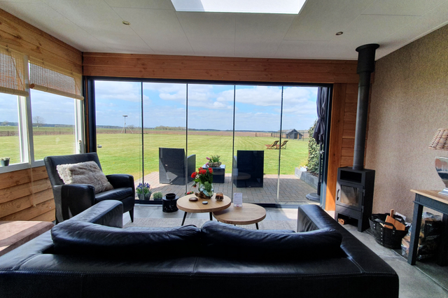 Ein Zimmer mit Sofa und Kamin mit Blick durch große Fenster auf die Felder.