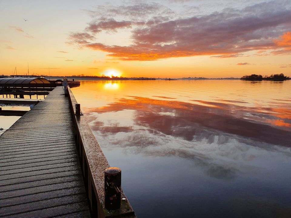 Houten steiger weerspiegeld in het stille water van de Loosdrechtse Plassen bij zonsondergang met paarse wolken.