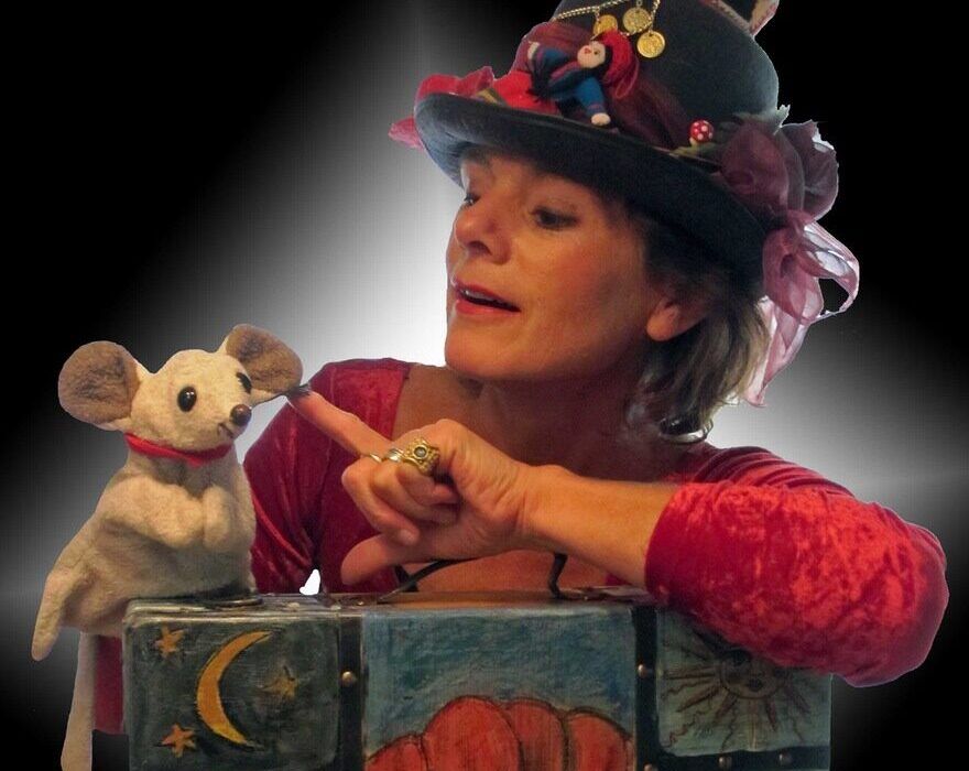 Foto van een mevrouw met een kleurrijk hoedje op en een handpop in de vorm van een muis.