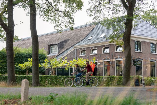 Een man en vrouw fietsen in een Drents dorp voor een oude boerderij langs.
