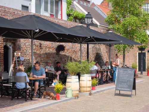 Langs de stadsmuur zitten mensen te eten en te drinken op een terras onder de parasol.